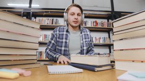 Student studying in a library with stacks of books and headphones on while taking notes at a wooden table during the day - Powered by Shutterstock - Get 15% off with code: PIKWIZARD15