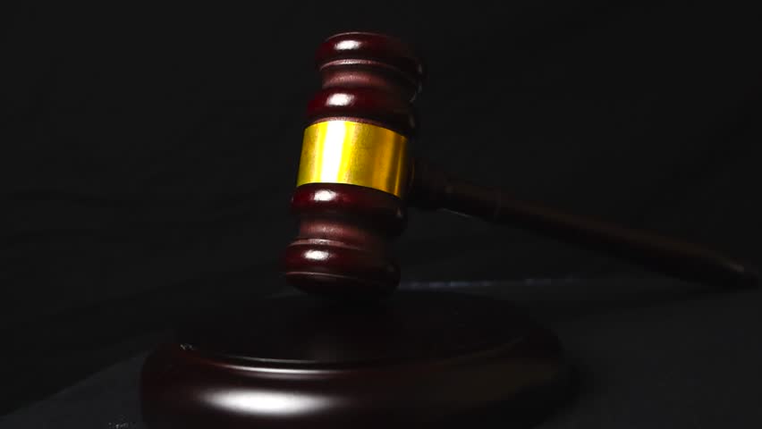 Close up view of a brown colored court justice hammer or gaol gavel placed in front of a black studio background. The gavel has bronze shiny and reflective metal decoration on it, good studio lights.