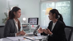 Two Asian businesswomen are discussing a project in a modern office, analyzing data on a tablet and paperwork - Powered by Shutterstock - Get 15% off with code: PIKWIZARD15