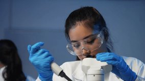 Professional scientist analyzing biological samples using precision microscope and pipette while wearing protective lab equipment in modern research laboratory - Powered by Shutterstock - Get 15% off with code: PIKWIZARD15
