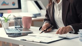 Businesswoman analyzing financial charts and typing on a laptop in a bright office, surrounded by documents, a smartphone, and a calculator - Powered by Shutterstock - Get 15% off with code: PIKWIZARD15