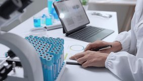 Medical researcher analyzing data on digital tablet, documenting findings with handwritten notes while standing near test tubes rack in modern laboratory setting - Powered by Shutterstock - Get 15% off with code: PIKWIZARD15