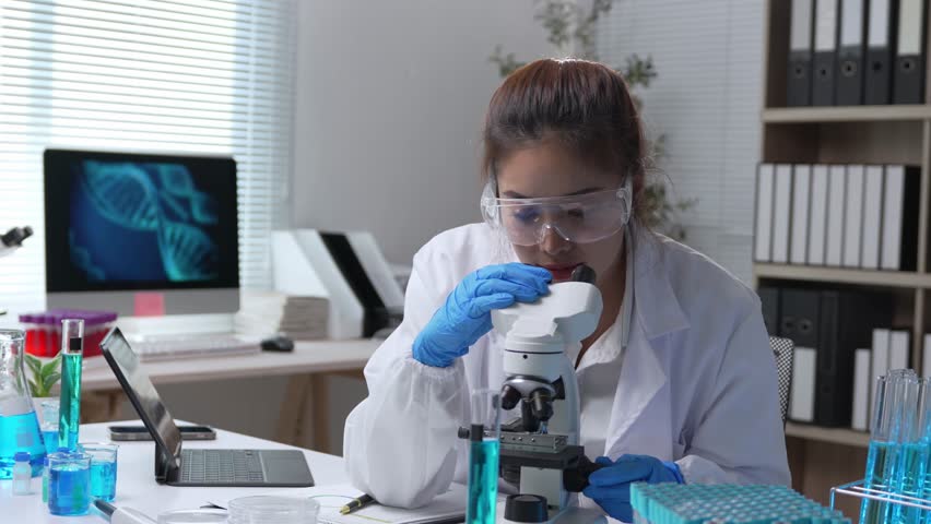 Professional female scientist in white coat and gloves using microscope, analyzing samples and liquids in modern laboratory with computer and dna structure on screen - Powered by Shutterstock - Get 15% off with code: PIKWIZARD15