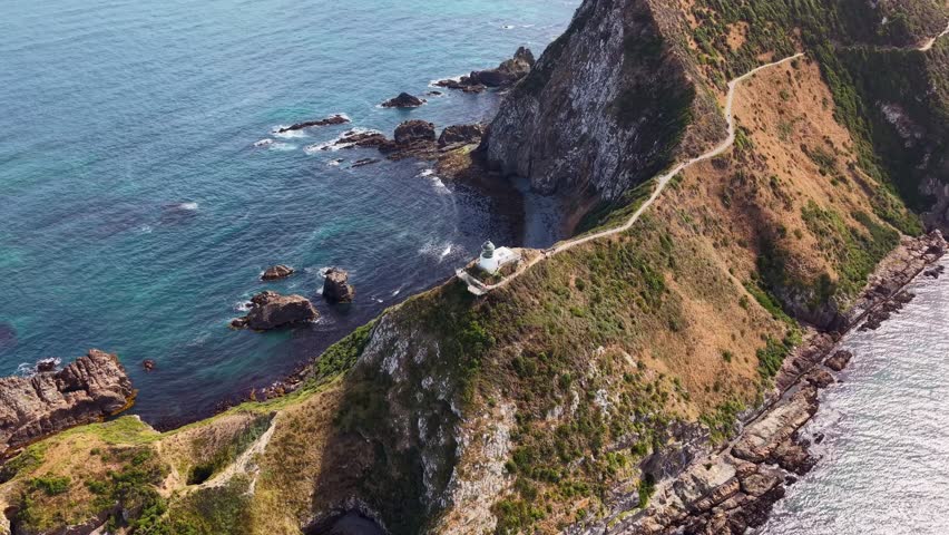 Drone orbit around Nugget Point lighthouse showing rocks, vast ocean and contrasting sea colors
