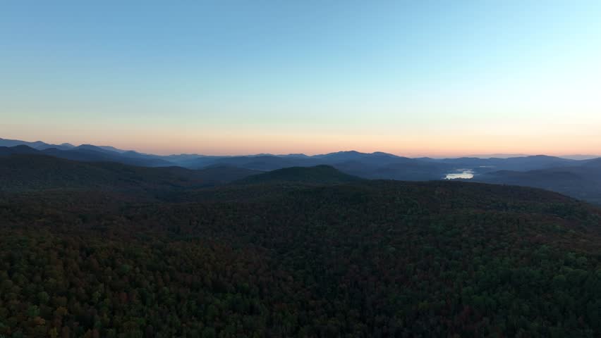 Aerial view of the Adirondack Mountains at sunrise under a clear sky with vibrant autumn colors.