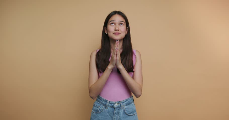 footage of young woman raising her hands in prayer conveys hope and aspiration, representing deep emotions on beige background