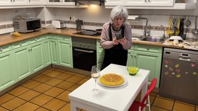 White haired woman proudly photographing homemade Spanish omelette in the kitchen with a glass of wine on the table - Powered by Shutterstock - Get 15% off with code: PIKWIZARD15