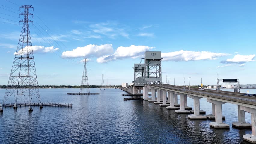 James River Lift Bridge JRB spans a calm waterway, supported by tall towers and visible cables. This infrastructure connects distant shores, reflecting on blue water beneath a bright, clear sky