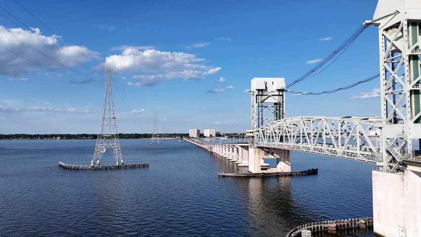 James River Lift Bridge JRB spans a calm waterway, supported by tall towers and visible cables. This infrastructure connects distant shores, reflecting on blue water beneath a bright, clear sky