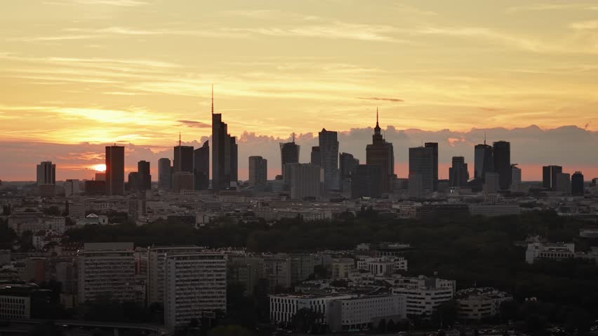 Aerial panorama of Warsaw city during golden hour at sunset. Cinematic drone shot of cityscape downtown silhouettes of skyscrapers modern architecture buildings on horizon, orange sunlight rays