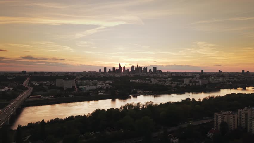 Wide angle aerial panorama of Warsaw city at sunset. Cinematic drone shot of cityscape downtown silhouettes of skyscrapers modern architecture buildings on horizon and car driving highway bridge