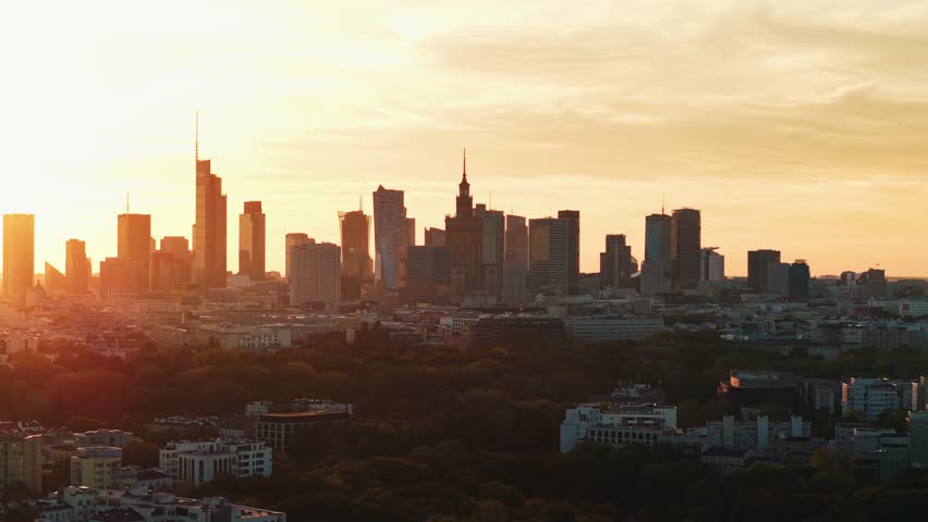 Aerial panorama of Warsaw city during golden hour at sunset. Cinematic drone shot of cityscape downtown silhouettes of skyscrapers modern architecture buildings on horizon, orange sunlight rays