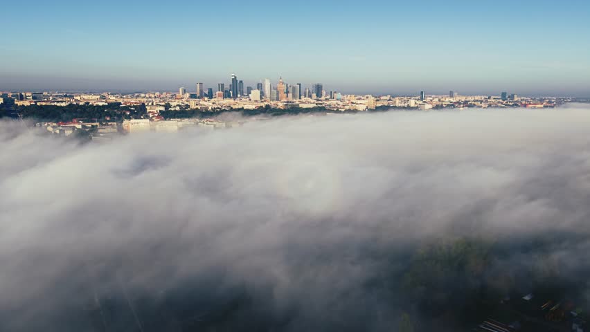 Wide angle aerial panorama of Warsaw city at foggy sunrise. Drone shot cityscape downtown skyscrapers modern architecture high-rise buildings on horizon, rolling clouds fog over Vistula river