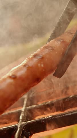 A professional chef is putting sausages on a grill grate over smoking coals for heat treatment of meat. Slow-motion footage