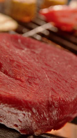 Panning down shot of an unknown person seasoning on top of a beef tenderloin, sprinkling coarse sea salt, pink and green peppercorns, and fresh herbs