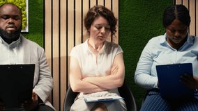 Diverse candidates group waiting in line in a corporate hallway with resumes, preparing for important interview with the hiring team. Reflecting nervousness and confidence. Camera B. - Powered by Shutterstock - Get 15% off with code: PIKWIZARD15