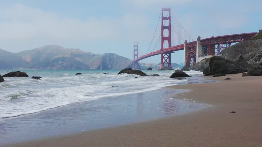 Waves roll onto sandy shore at Baker Beach with Golden Gate Bridge in background, San Francisco, California, USA. Iconic coastal view with ocean, rocks and Marin Headlands