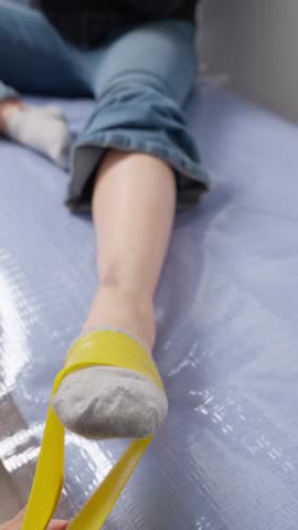 Young female patient undergoing physical therapy for an ankle injury. A physiotherapist is using a yellow resistance band to stretch her foot