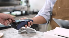 Senior entrepreneur cafe owner barista holds POS terminal while customer swipes creditcard, Asian retired female in apron smiling at counter, demonstrating cashless payment inside modern coffee shop - Powered by Shutterstock - Get 15% off with code: PIKWIZARD15