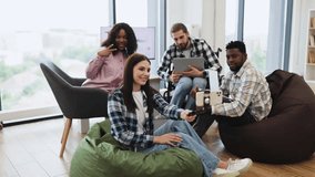 Group of diverse young adults sitting on beanbags in bright modern office posing for selfie. Relaxed and cheerful atmosphere. Ideal for concepts of teamwork, friendship, and modern workplace dynamics. - Powered by Shutterstock - Get 15% off with code: PIKWIZARD15