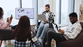 Young adult man in wheelchair presenting in office environment with diverse coworkers using technology displays - Powered by Shutterstock - Get 15% off with code: PIKWIZARD15