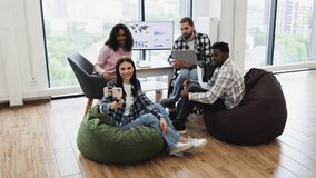 Young diverse coworkers relaxing on beanbags, taking selfie using smartphone, enjoying modern office. Multiracial group of adult friends casually interacting, inclusive team-building - Powered by Shutterstock - Get 15% off with code: PIKWIZARD15