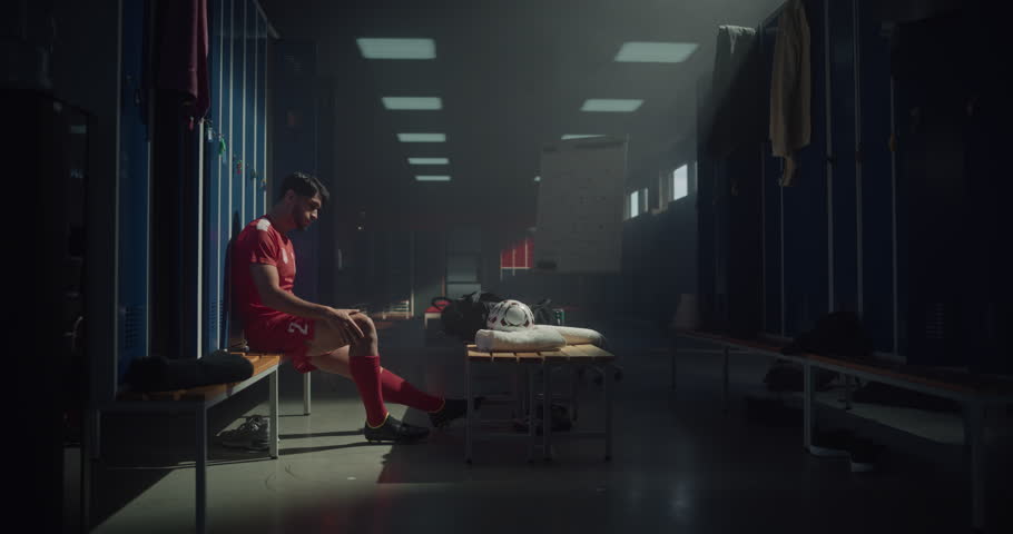 Soccer Player Sitting Alone on a Locker Room Bench, Holding His Leg in Pain After an Injury. Athlete Shows Frustration and Discomfort, Reflecting the Struggle of Sports Injuries During a Football Game
