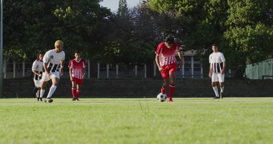 Football attacker dribbling ball down center pitch evading defender lunging slide and turf spraying. Athletes, competition, agility, sports, action, outdoor, teamwork