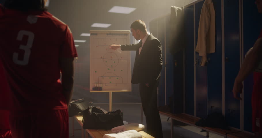 Soccer Coach Standing in Front of His Team in the Locker Room, Pointing at a Whiteboard with a Plan. Football Players Listen Attentively as He Explains the Game Strategy and Tactics