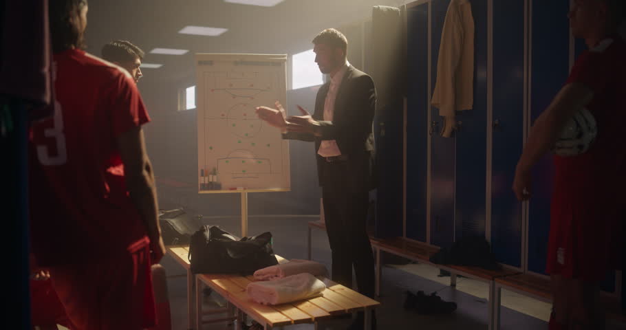 Soccer Coach Standing in Front of His Team in the Locker Room, Pointing at a Whiteboard with a Plan. Football Players Listen to Game Strategy and Tactics, Making High Fives to Encourage the Team