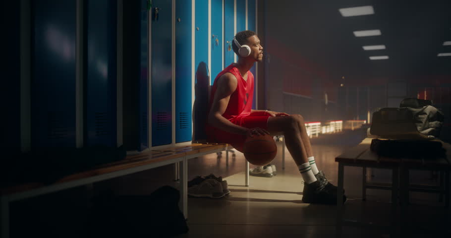 Black Basketball Player Sitting Alone in Locker Room, Listening to Music on Headphones while Bouncing the Ball with Precision. Athlete Focuses and Prepares Mentally Before the Game