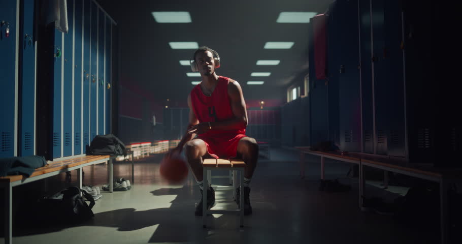 Black Basketball Player Relaxing on Bench, Listening to Music and Practicing Ball Tricks by Spinning It on His Finger. Moment Highlights Skill, Concentration and Mental Preparation for the Game