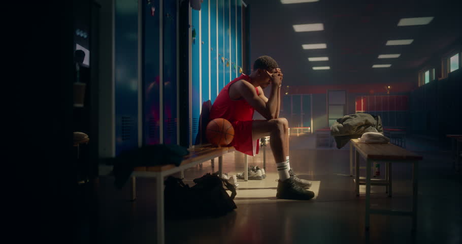 Black Basketball Player Sitting Alone on a Locker Room Bench, Looking Upset After a Tough Game. Teammate Approaches, Patting His Shoulder and Offering Words of Encouragement