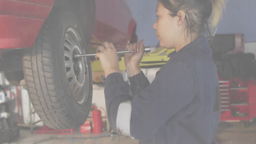 Female mechanic grabbing wrench at auto shop, loosening lug nuts checking wheel with torque charts. Mechanic, automotive, repair, industrial, tools, workspace, precision