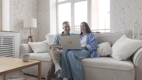 Middle aged man with gray hair and young adult brunette woman in casual clothes sitting on sofa with laptop, discussing with light smiles and focus. Positive atmosphere of teamwork at home - Powered by Shutterstock - Get 15% off with code: PIKWIZARD15
