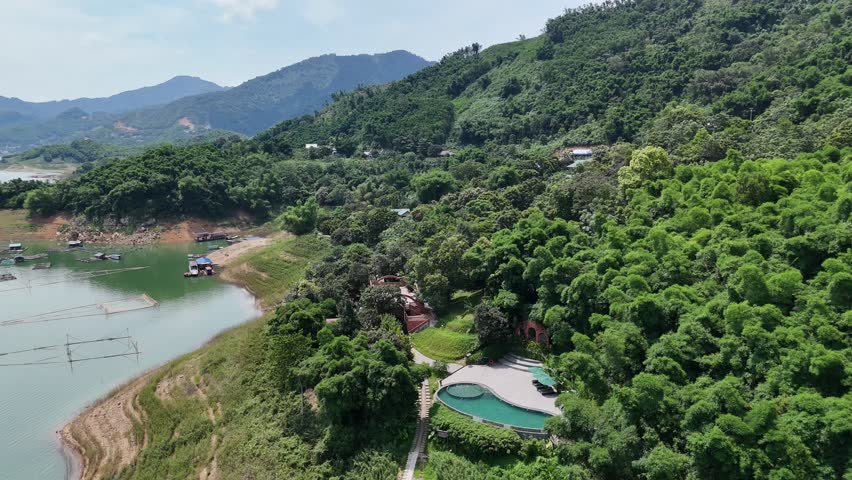 Aerial footage of the lakeshore with sandy banks, dense green forest, and mountains in the distance.