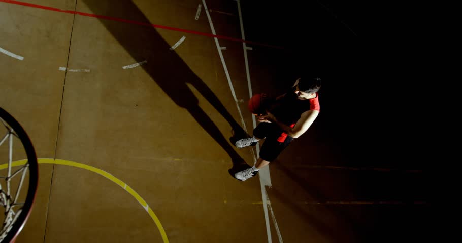 Player bouncing ball and sizing up hoop under spotlight in training, jumping and shooting to score. Athletic, action, dynamic, focus, performance, sport, energy