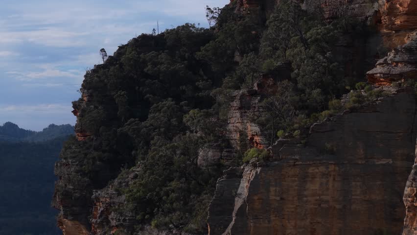 Aerial soars along forested cliffs with sun-drenched ridgelines and shadowed valleys below, Blue Mountains NSW Australia reveal of landscape