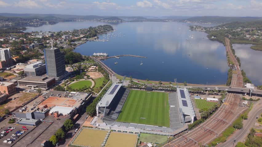 Wide aerial ascend orbit of Polytech Stadium in Gosford with visible stands, field, and nearby coastline, Central Coast NSW Australia