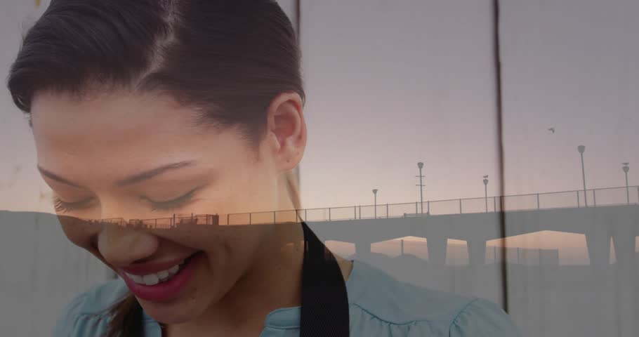 Woman raising vintage camera and turning winding knob for education showing sunset pier overlay. Nostalgia, artistry, craftsmanship, documentary, introspection, serenity, timeless