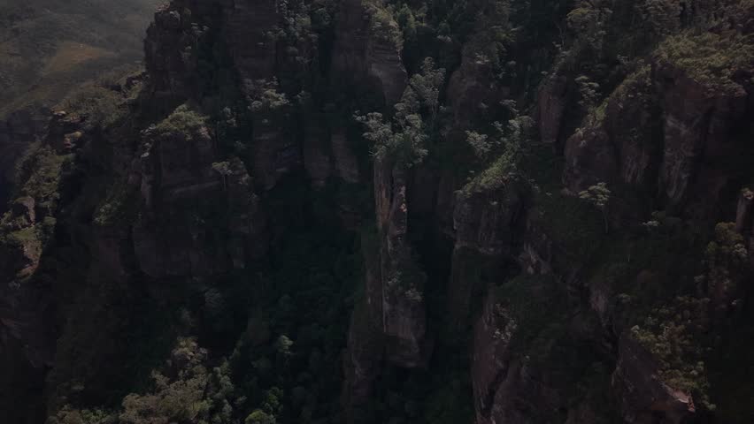 Dramatic drone overview of rocky outcrops and dense gum forests, warm sunset tones across range, Blue Mountains NSW Australia