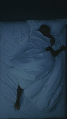 Adult African American Man Turns Restlessly in Bed, Suffering From Insomnia, Obsessive Thoughts, Anxiety. Concept Tiredness, Mental Unhealthiness, Poor Sleep, and Low quality Rest. Vertical Shot.