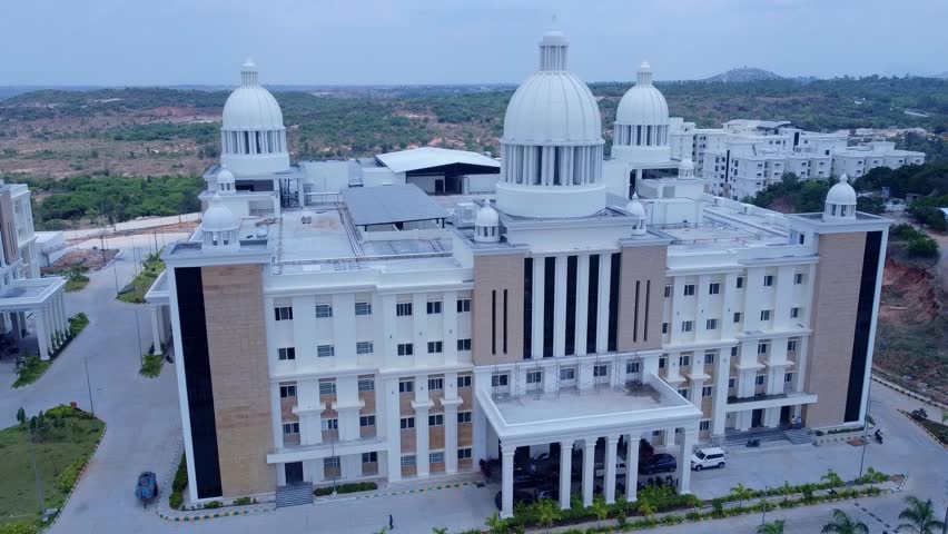 Aerial pull-back shot revealing the majestic, neo-classical main building and campus of Kanha Shanti Vanam, a large spiritual and meditation center in Telangana, India, set in a hilly landscape.