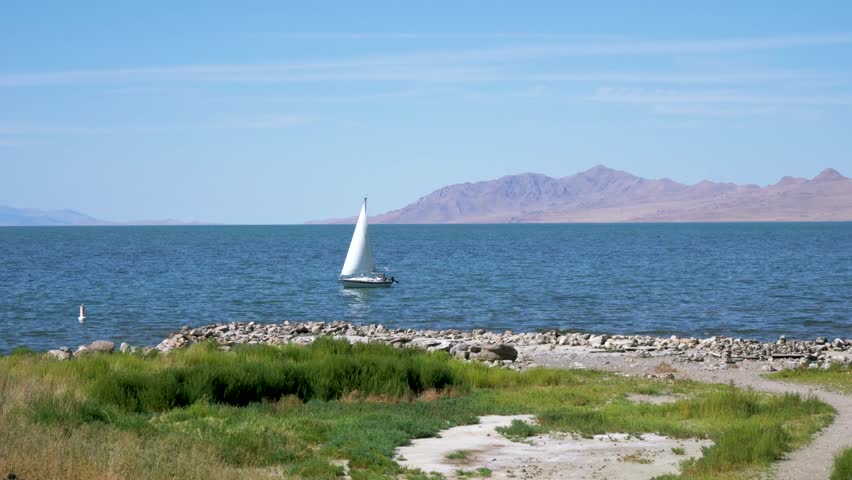 Sailboat uses wind to glide by rocky shore of The Great Salt Lake in Utah