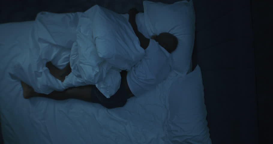 At Night, Man in Bed Has Restless Dreams. Adult African American Man on Snow white Bed Tosses and Turns. Concept of Nightmares, Poor Sleep, and Exhaustion After Hard Days Work. Rotating Top View.
