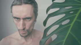 Skeptical Cunning Funny Big-Headed Guy with Monstera Plant in Close-Up, Intense Gaze, Soft Lighting, and Mood Atmosphere - Powered by Shutterstock - Get 15% off with code: PIKWIZARD15