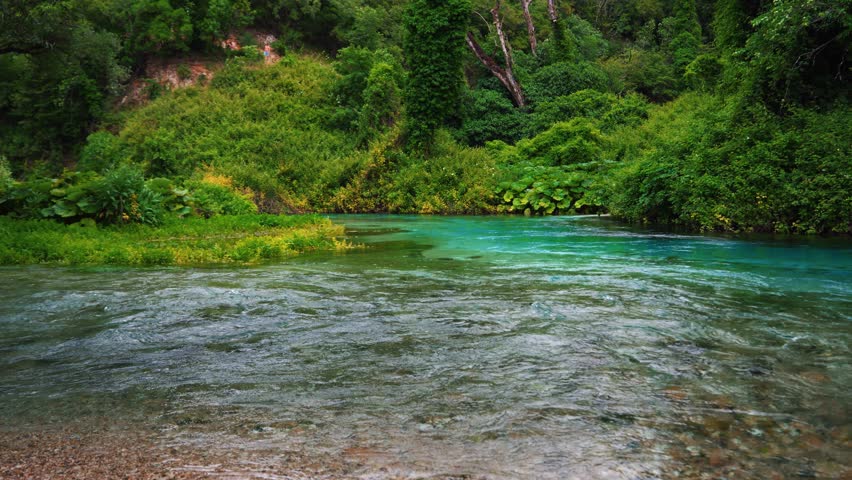 Flowing river at Albania’s Blue Eye spring with crystal clear turquoise water and green banks.