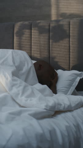 In Morning Handsome African American Man Wakes Up in Bed Sound of Alarm Clock. Guy Gets Out Bed, Squinting Eyes Against Bright Sunlight. Concept Morning Awakening, Everyday Morning. Vertical Shot.