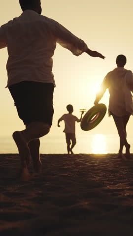 Little boy playing with toy plane and running on beach, mom and dad running near . Happy family spending weekend together and having fun on sea coast in summer vacation, be happy and feel joy