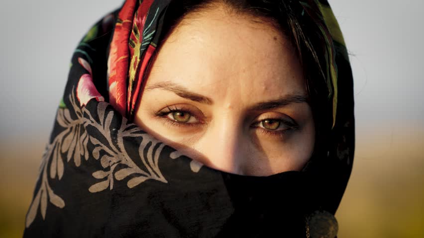 Close-up portrait of a young arab woman with beautiful hazel eyes wearing a traditional floral headscarf, looking directly at the camera